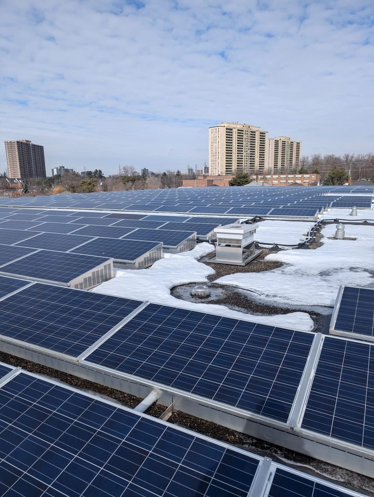 Rooftop solar array in winter with apartment towers behind
