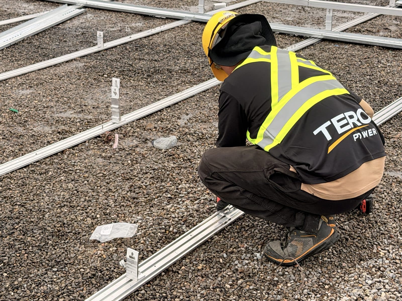 Tero Power installer in a hard hat and high-visibility vest fastening racking on a gravel roof