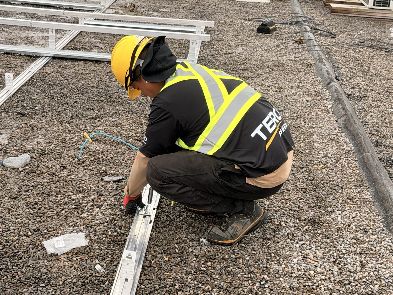 Close-up of a Tero Power installer fastening a racking rail on the gravel roof