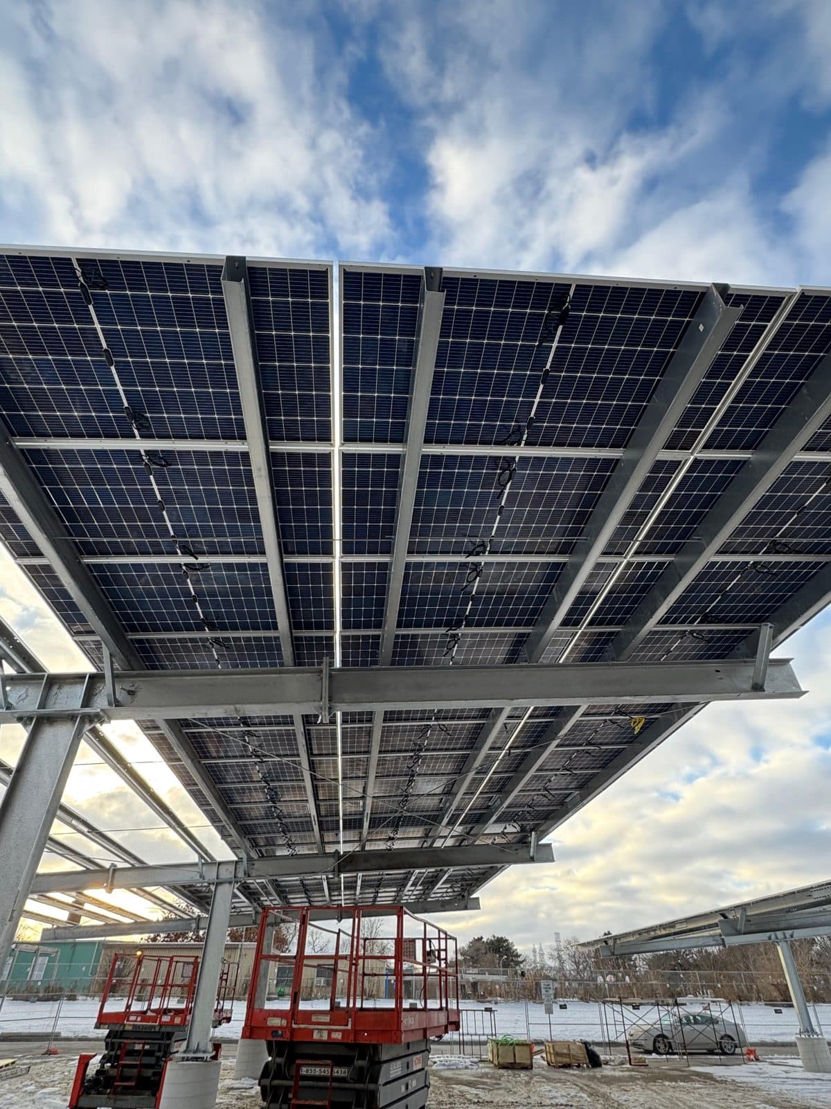 Solar carport structure under construction, seen from below with a scissor lift